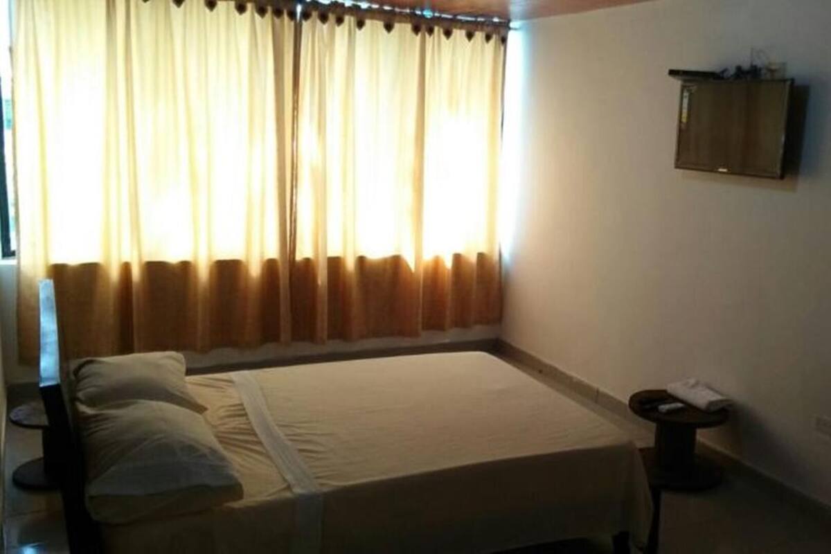 Een hotelkamer met een bed, nachtkastje, een kleintje tafeltje met stoel, en een wandkast.