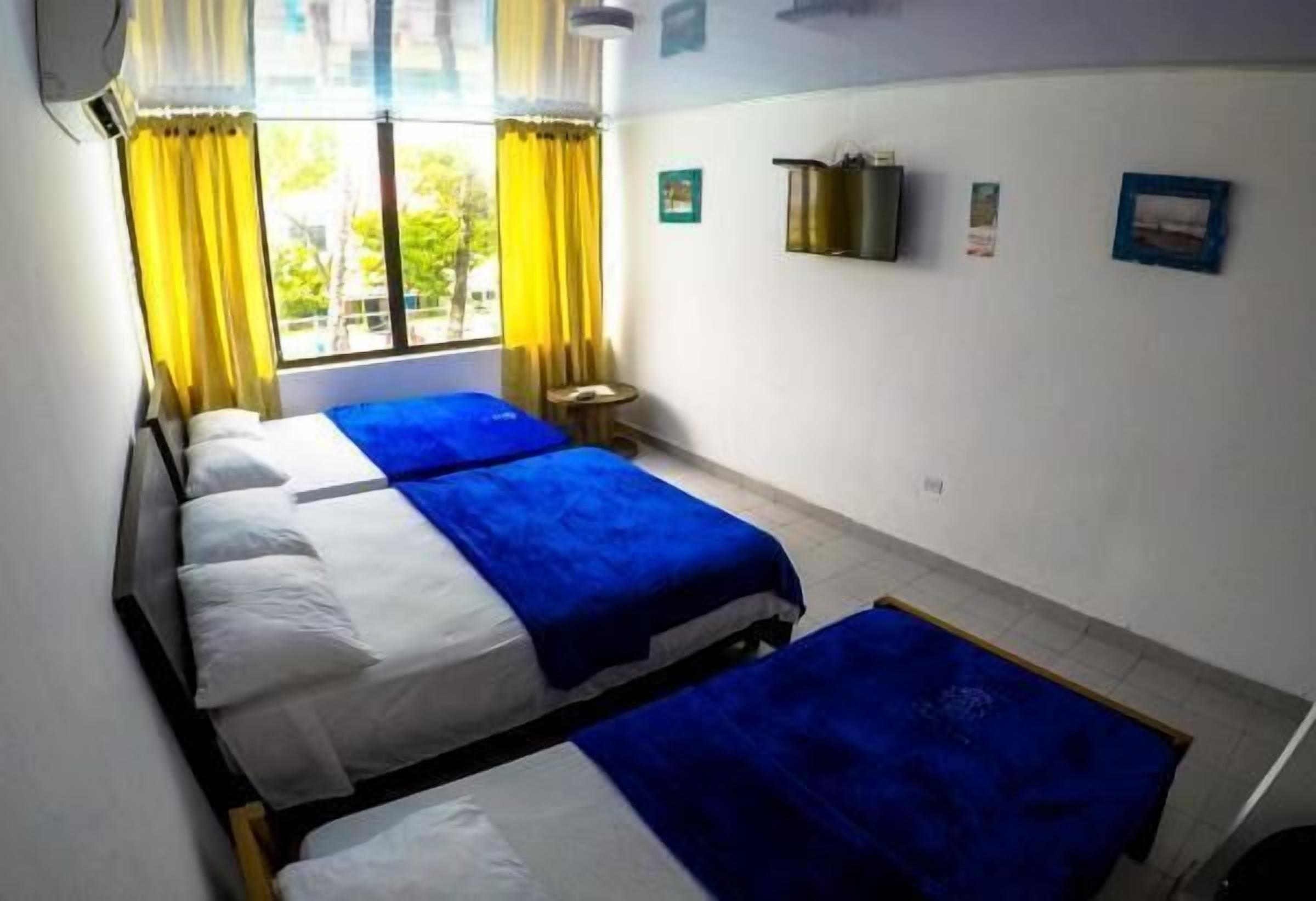 A room with three beds, a small table, and a window with curtains.