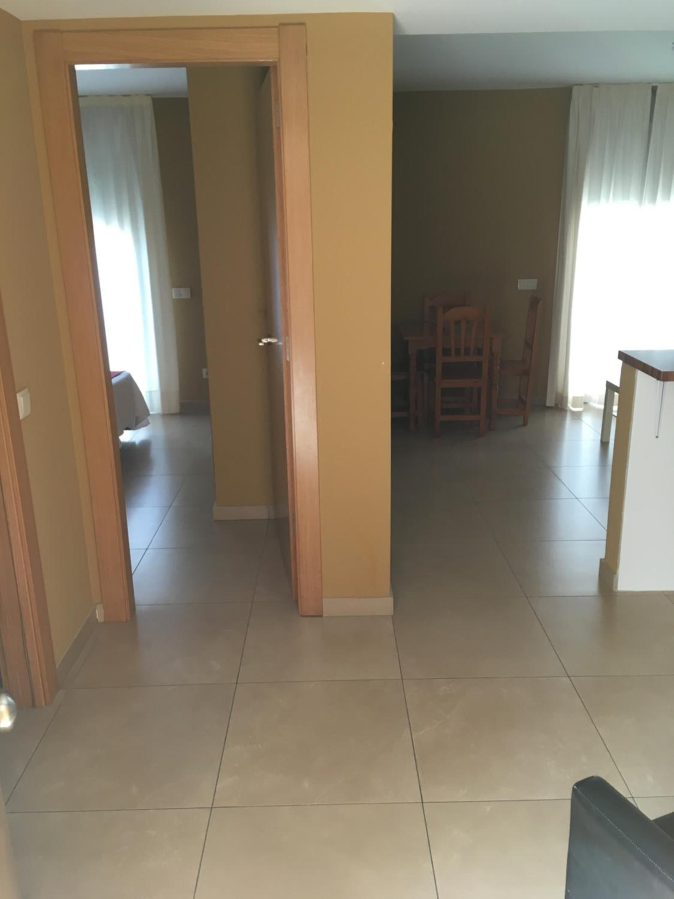 A spacious living area with a tiled floor, a wooden door, and a dining area with chairs and a table.