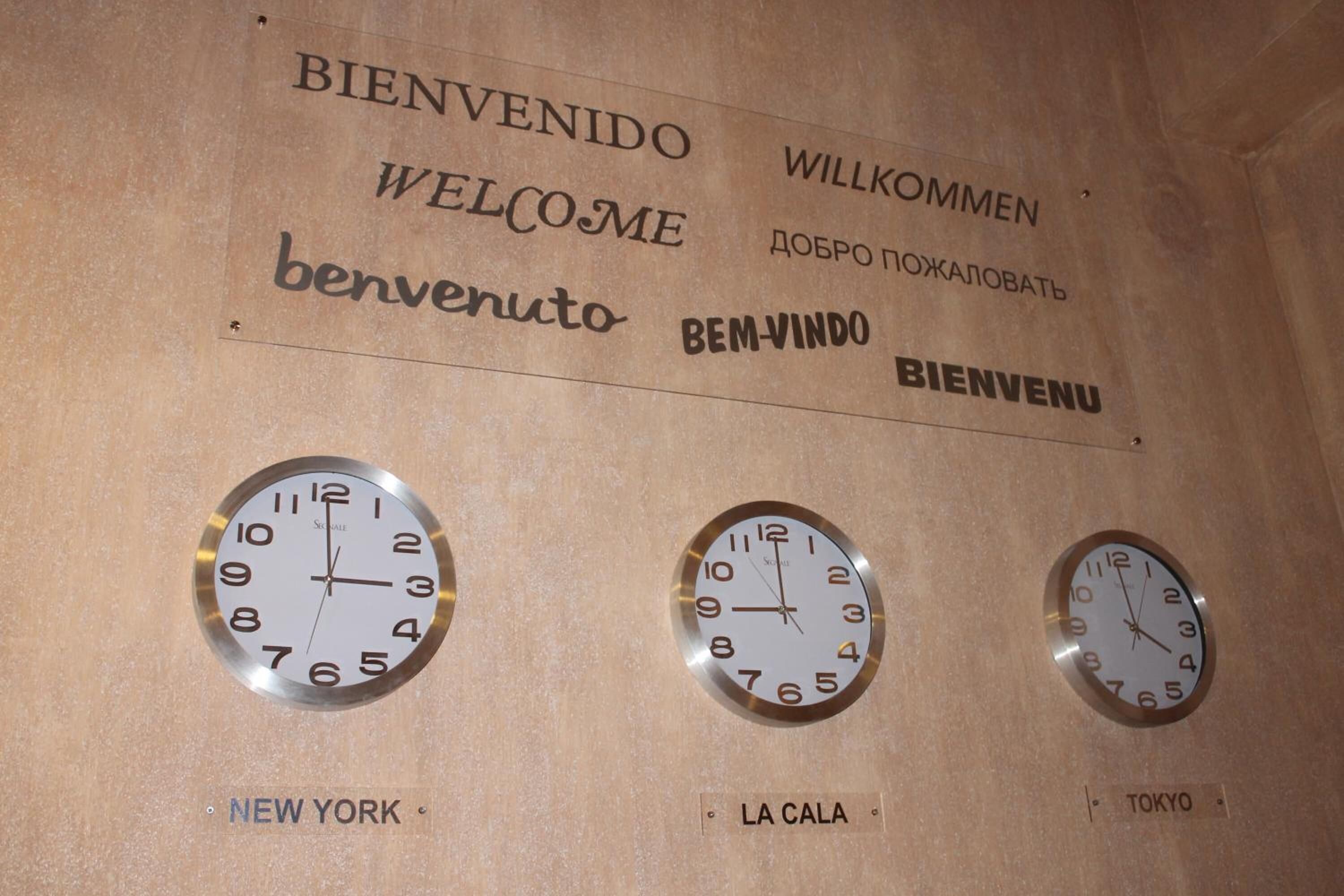 A wall with clocks and multilingual welcome signs.