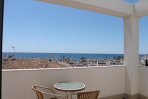 A balcony with a table and chairs, overlooking a coastal town and the sea.