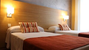 A hotel room with two beds, each with a striped pillow and a red blanket. There are wall-mounted lights on either side of the headboard. - Hotel Carmen (Mijas)