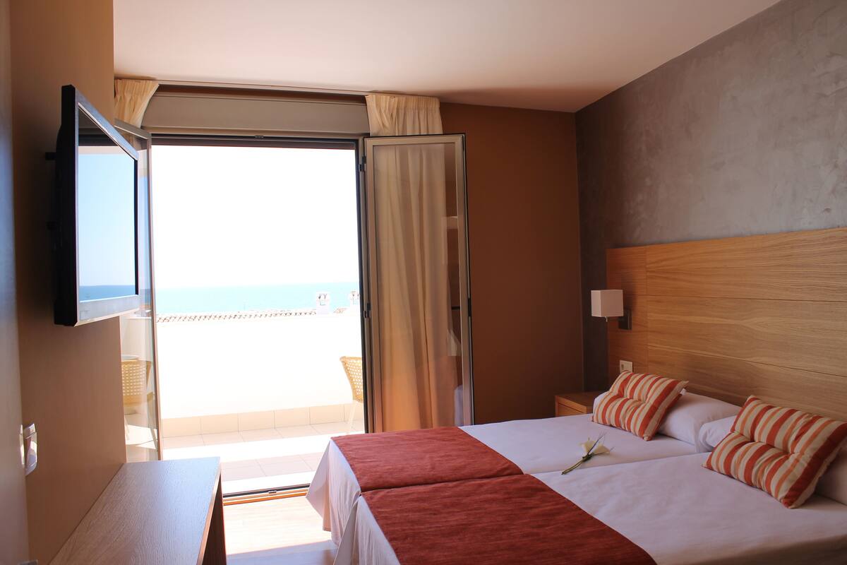 Une chambre d’hôtel avec un balcon, un lit agrémenté d’oreillers à rayures et un téléviseur fixé au mur.