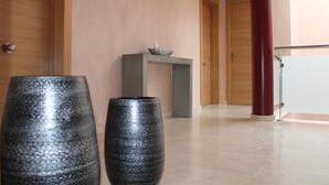 A modern lobby with a wooden door, a grey console table with a decorative bowl, and two large black vases. - Hotel Carmen (Mijas)