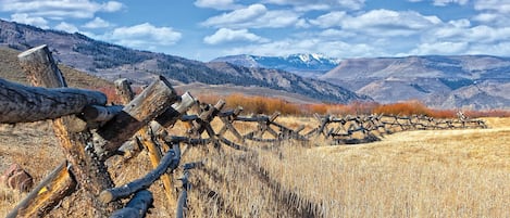 Une clôture en bois rustique se dresse dans un champ d’herbes sèches, avec des montagnes en arrière-plan.