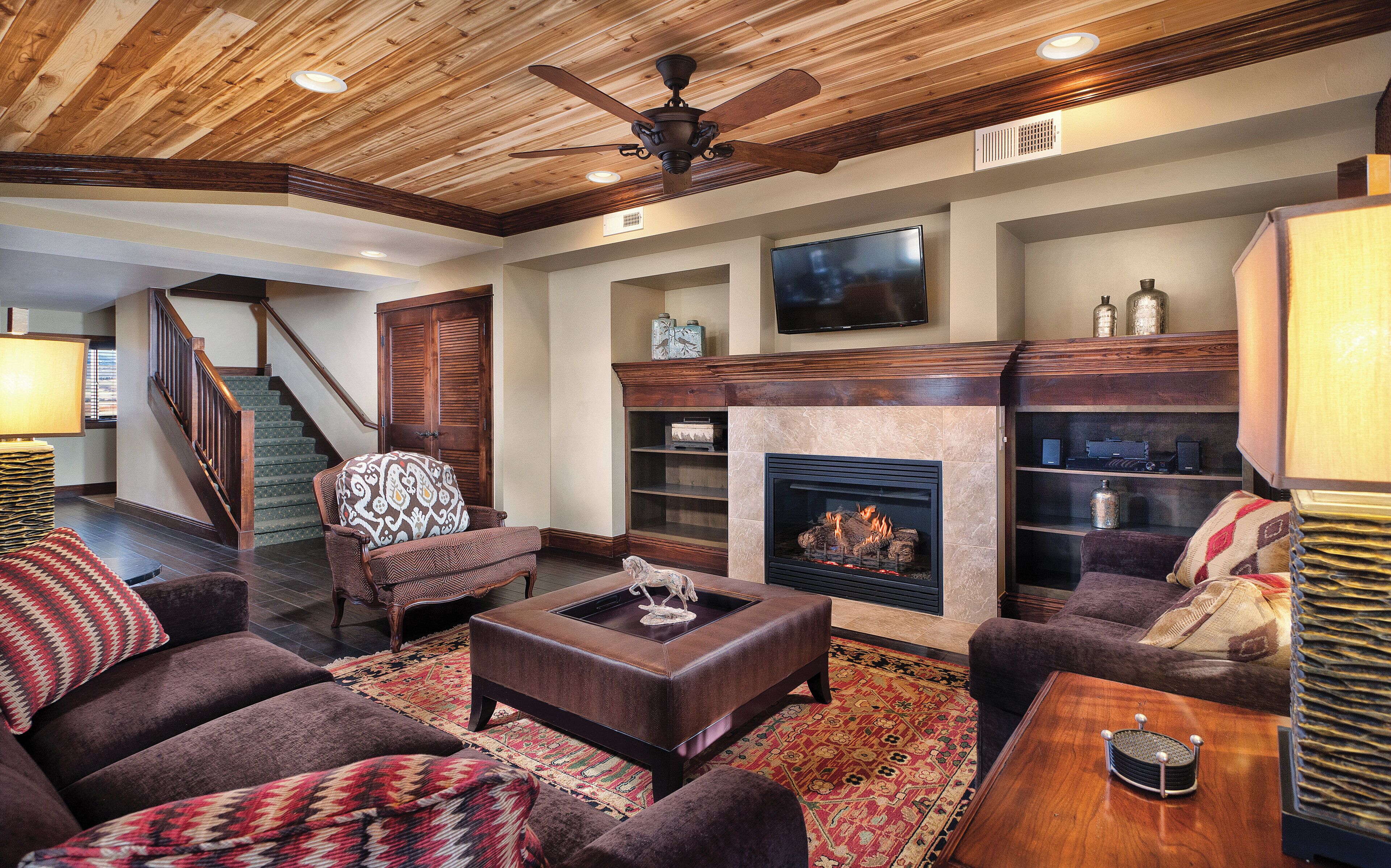 A living room with a fireplace, a television mounted above it, and a ceiling fan.