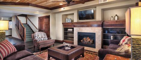 A living room with a fireplace, a television mounted above it, and a ceiling fan.