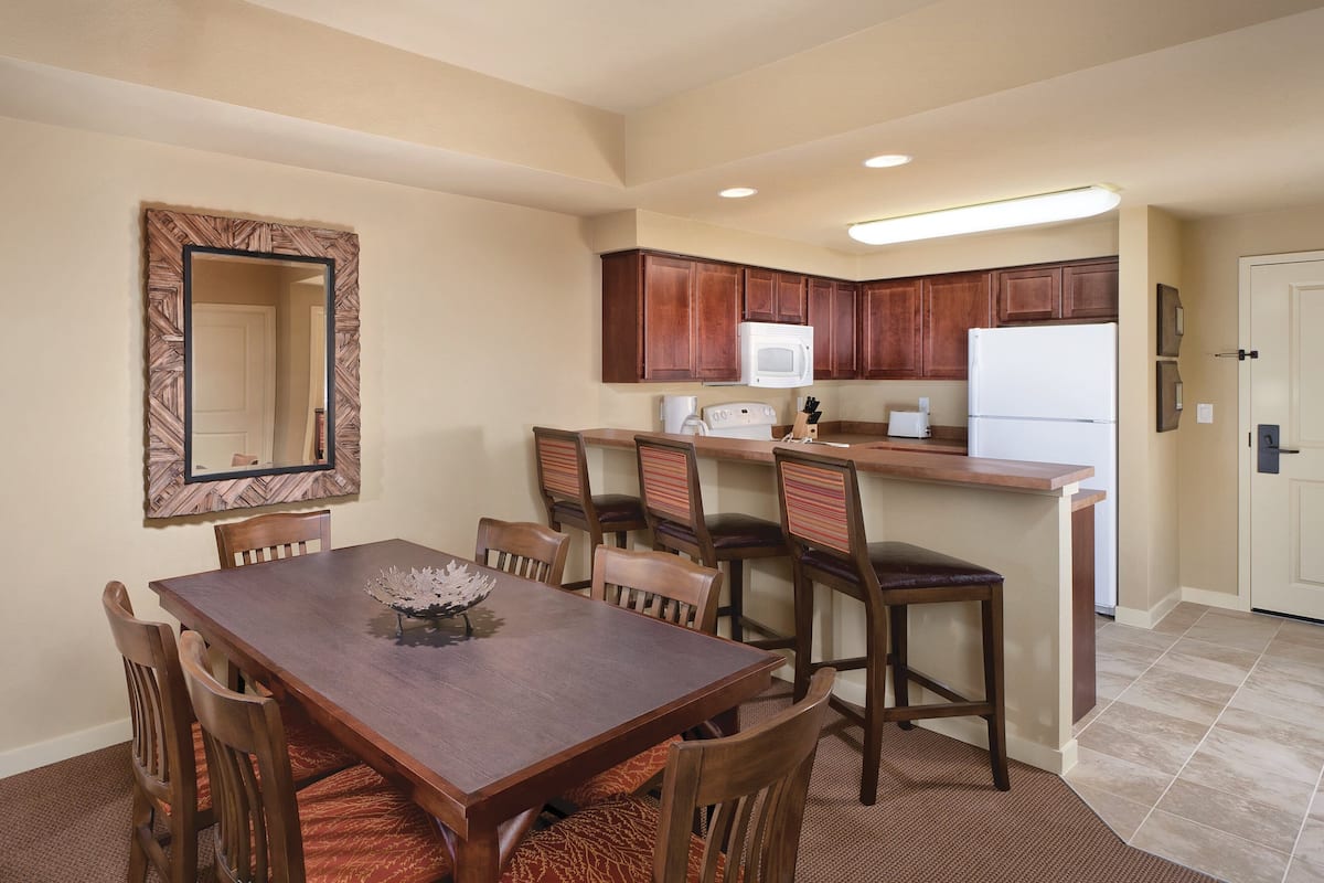 A dining area with a wooden table and chairs, a kitchen with wooden cabinets and appliances, and a mirror on the wall.