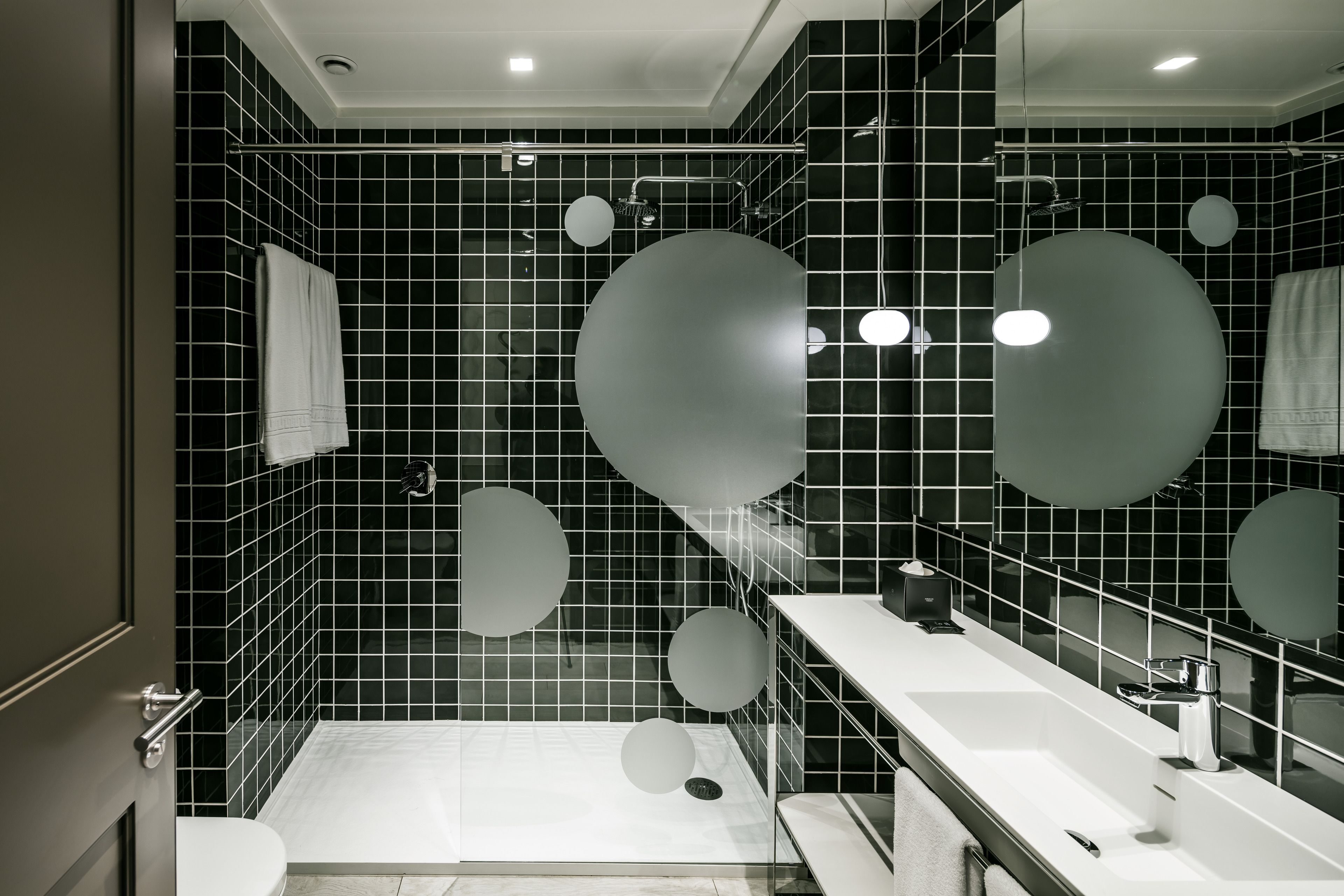 A modern bathroom with black tiled walls, a white sink, and a large mirror.