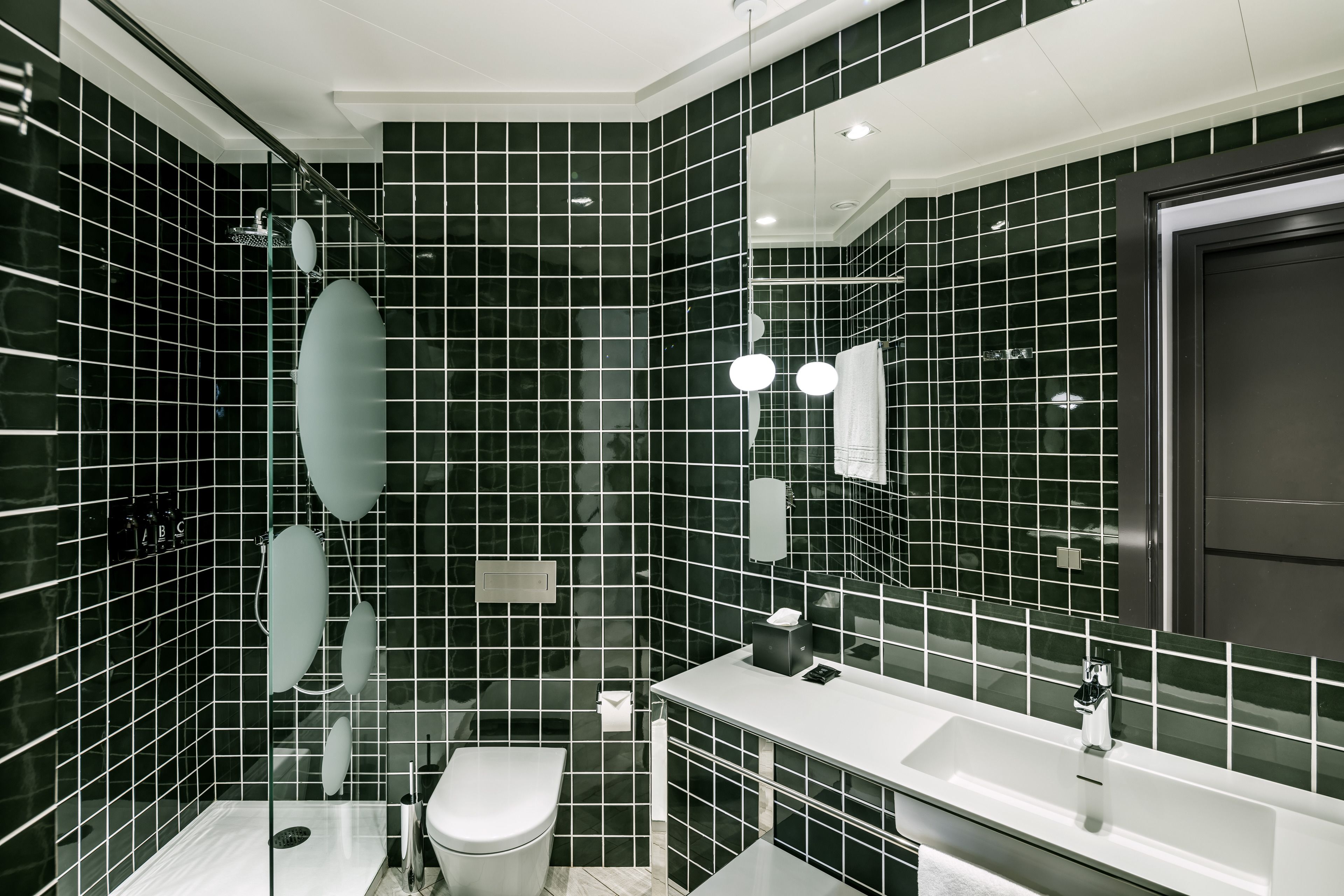 Un baño moderno con paredes de azulejos negros, un lavamanos blanco y una ducha con mampara de vidrio.