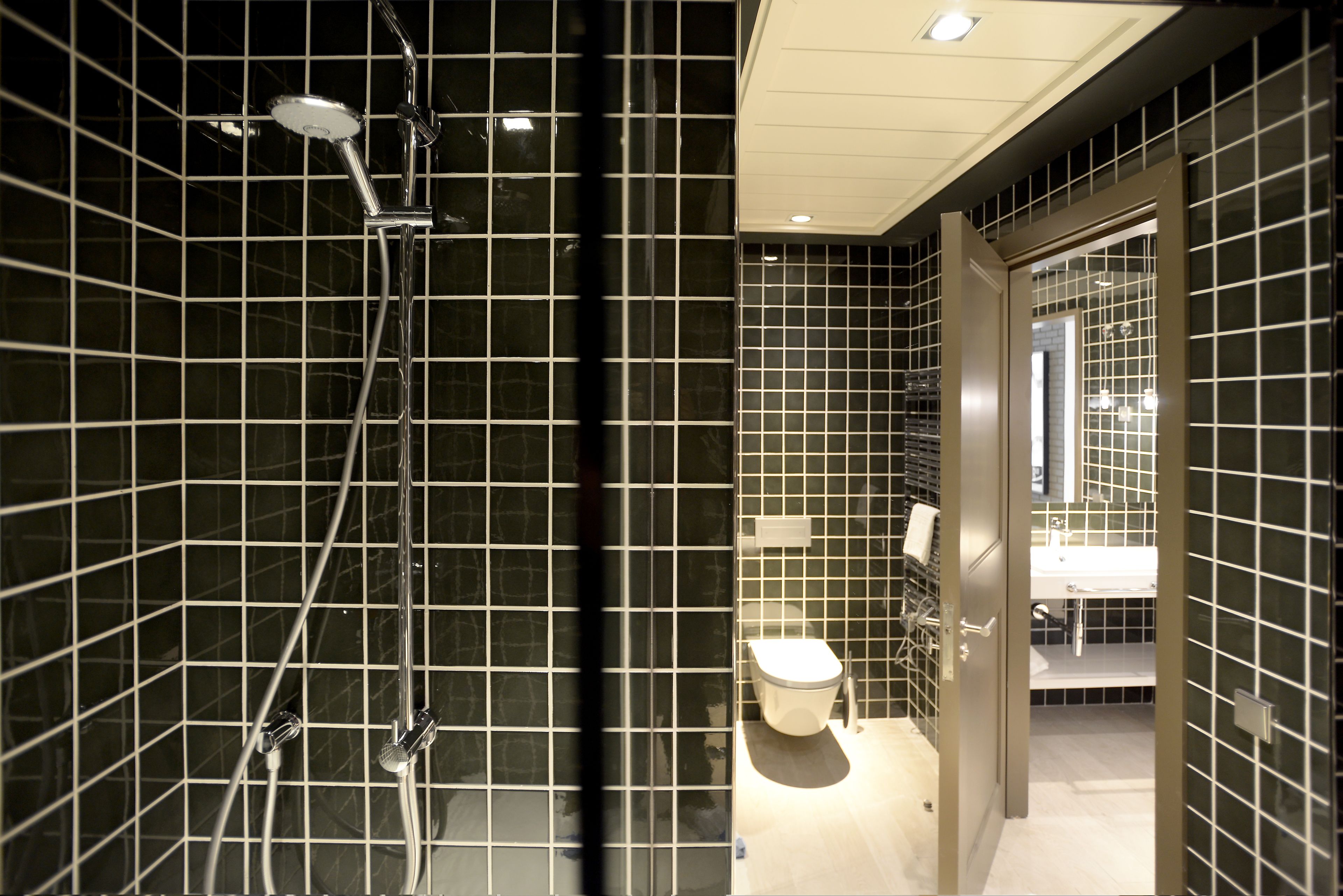 Ein modernes Badezimmer mit schwarzen Fliesenwänden, einem sichtbaren Duschbereich und einem Waschbecken mit Spiegel.