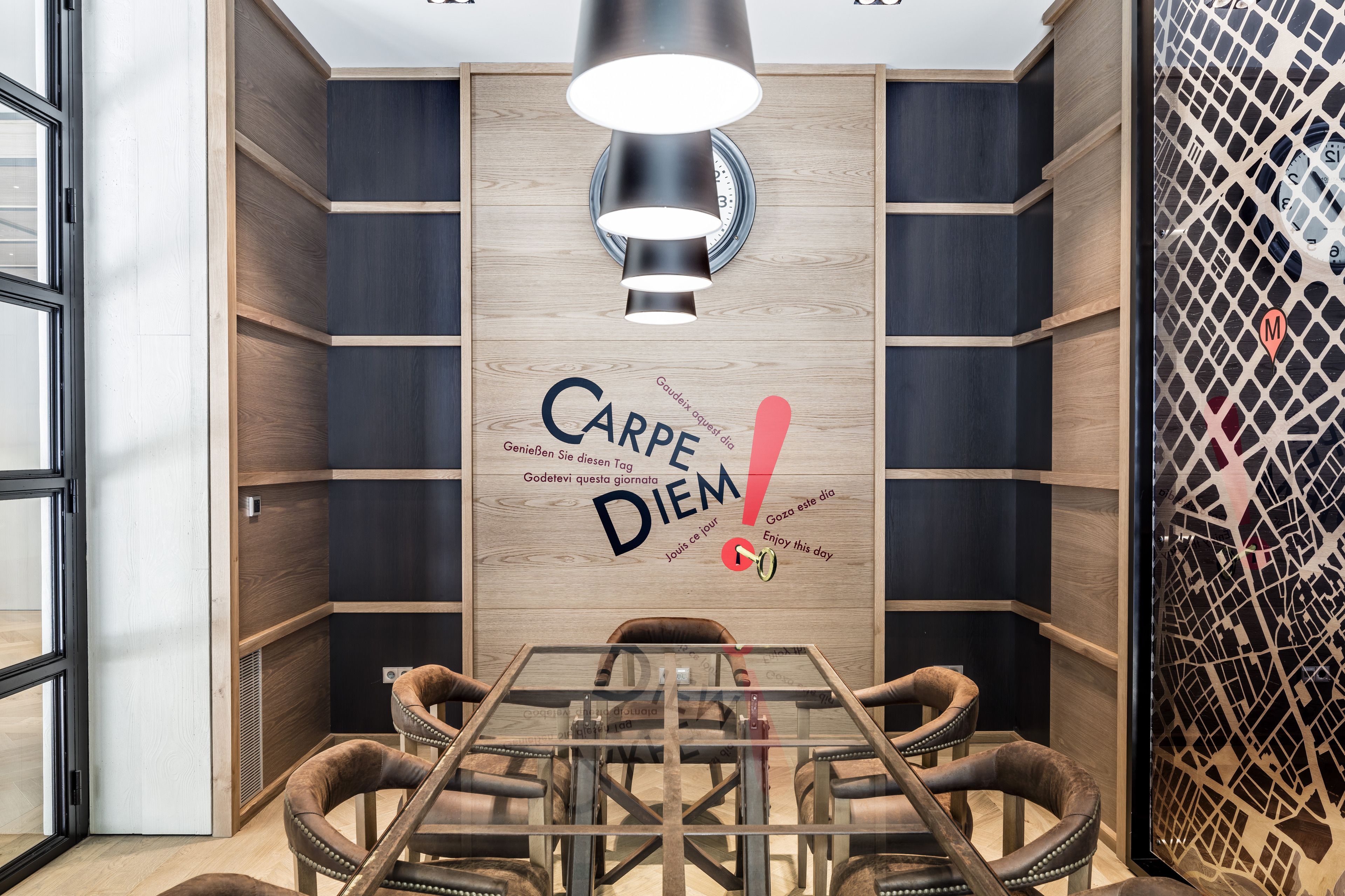 A modern conference room with a glass table, wooden chairs, and a wall with multilingual motivational text.
