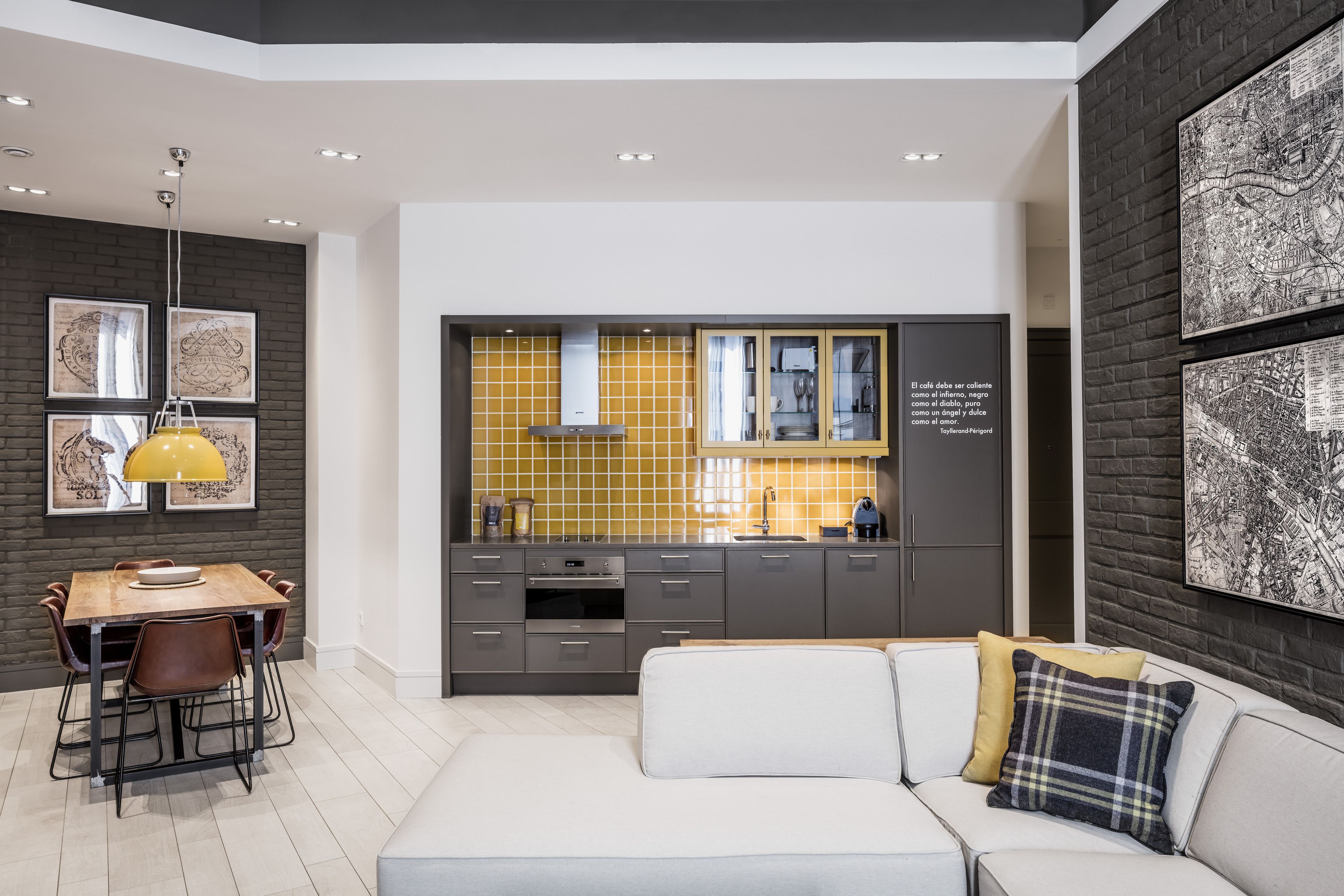 A modern kitchen with a central island, a dining area with a table and chairs, and a living area with a sofa and cushions.
