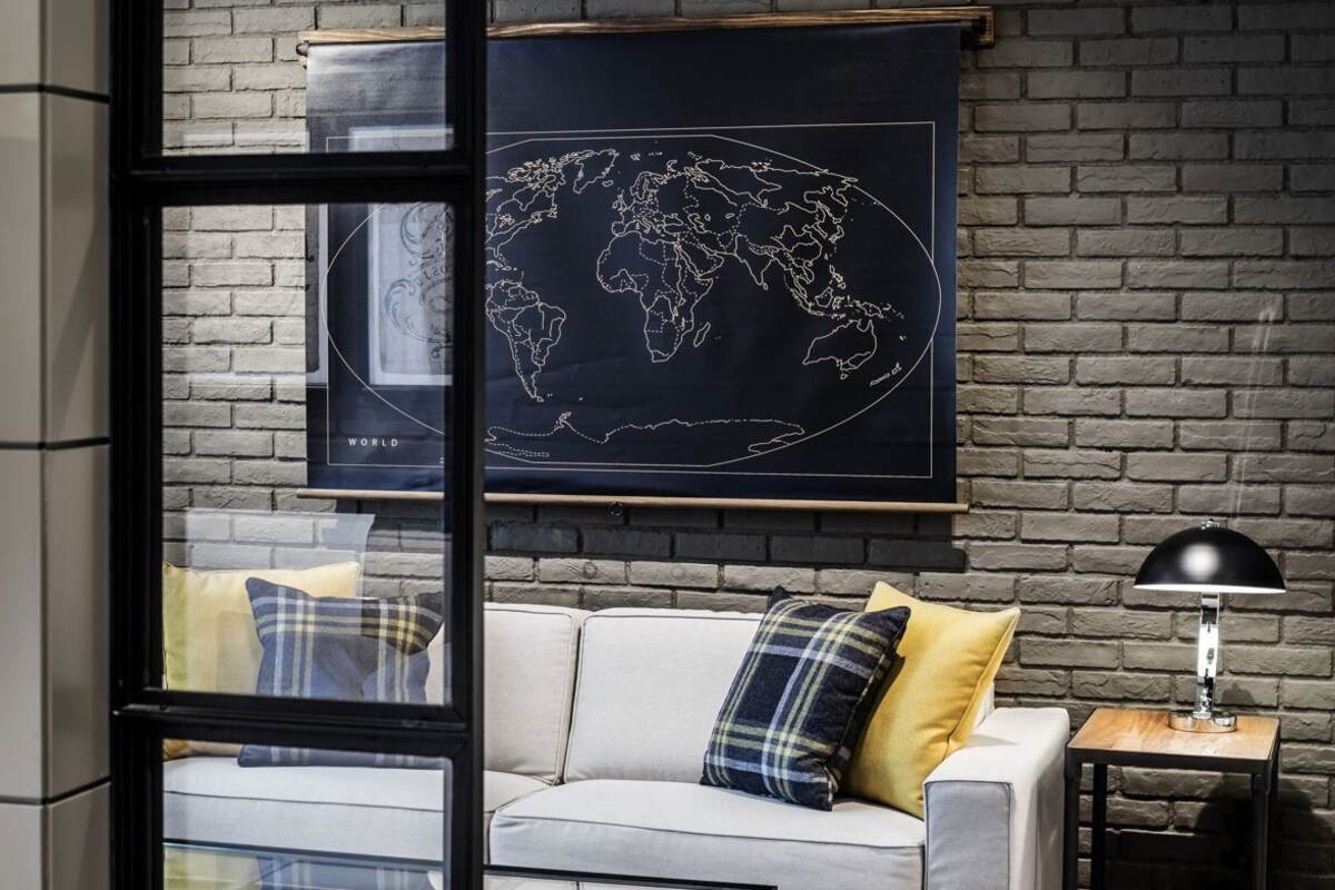 Una sala de estar moderna con un sofá, una mesa de centro de vidrio, un mapa del mundo en la pared y una lámpara sobre una mesita.