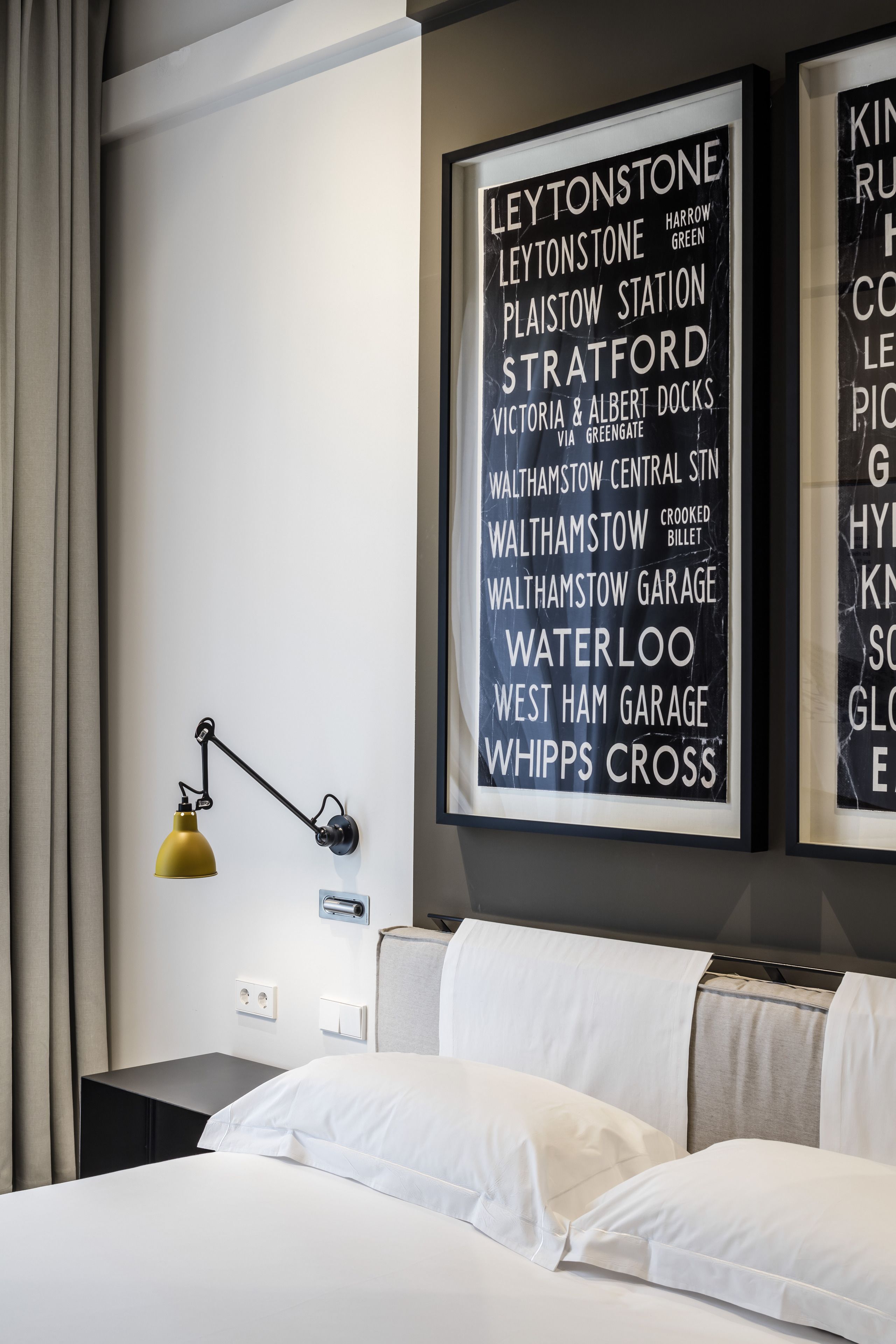 Una habitació d'hotel amb un llit, una tauleta de nit, una làmpada i una paret amb una llista de noms.