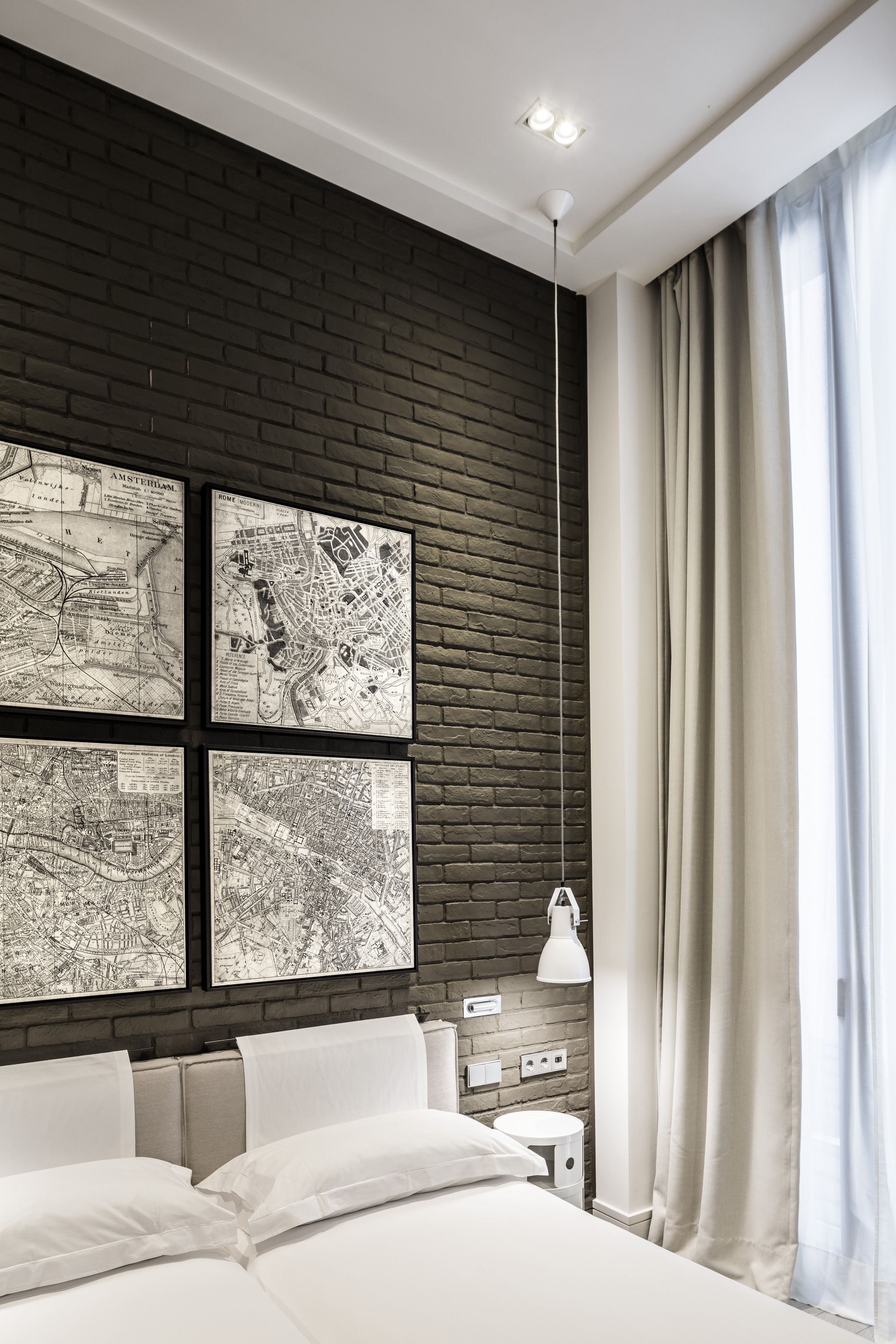 A modern hotel room with a brick accent wall, a large bed, a nightstand, a lamp, and a window with curtains.