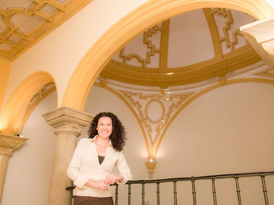 A woman standing on a staircase with ornate architectural details and a railing.
