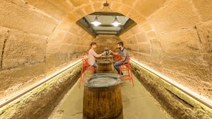 A stone-walled room with two people seated at a wooden table with a glass top, under a hanging light fixture. - Teatrisso Hotel Palacio (Cuzcurrita de Rio Tiron)