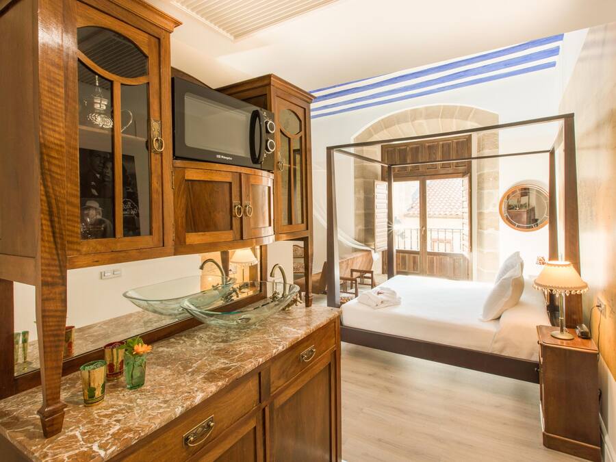 A hotel room with a wooden cabinet, a glass bowl sink, a bed, and a view of the outside.