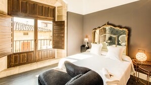 Habitación de hotel con una cama grande, un armario de madera, un balcón con vistas a la ciudad y un espejo decorativo en la pared.