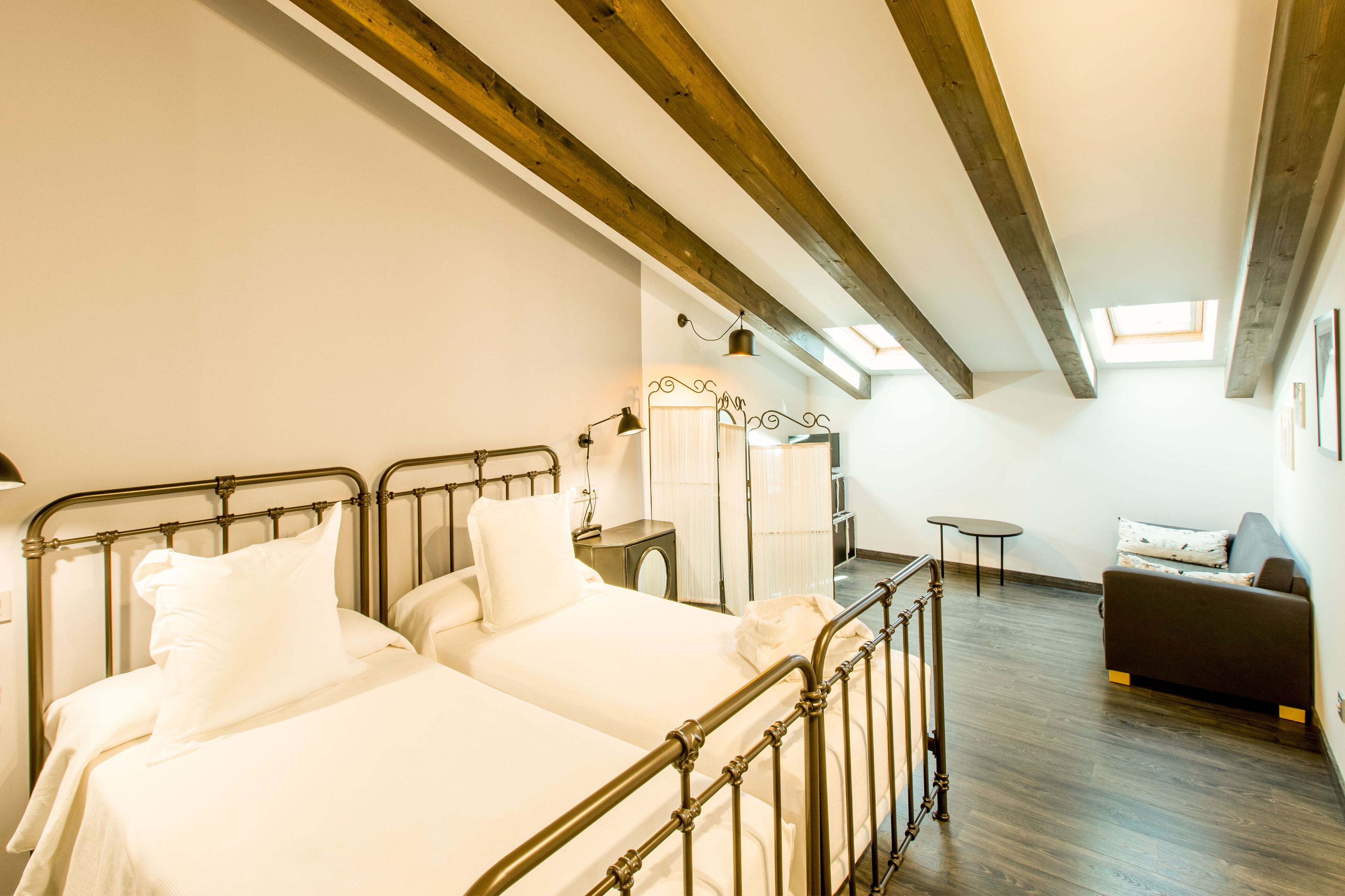 Un dormitorio con dos camas, una mesita, un sofá y un tragaluz.