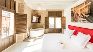 A bedroom with a large bed, a bathtub, and a stone wall. - Teatrisso Hotel Palacio (Cuzcurrita de Rio Tiron)