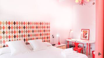 A modern hotel room with a large bed, a desk with a chair, a small table, and a wall with a geometric pattern.