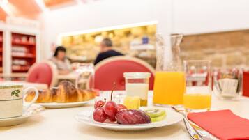 A breakfast setting with croissants, grapes, kiwi, and orange juice on a table.