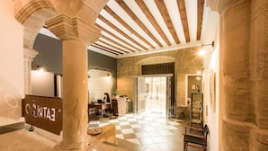A lobby with stone columns, a checkered floor, a reception desk, and a view into the dining area. - Teatrisso Hotel Palacio (Cuzcurrita de Rio Tiron)