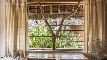 A room with a wooden table, a fan, and a window with a thatched roof view.