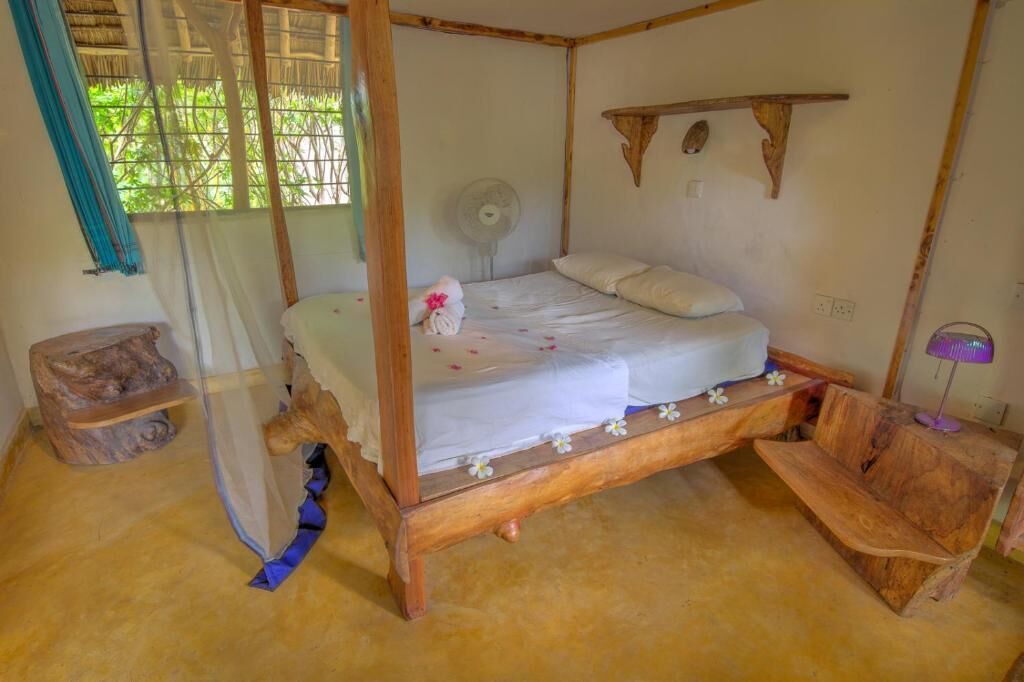 Una cama con dosel, un ventilador de noche y una pequeña estantería de madera.