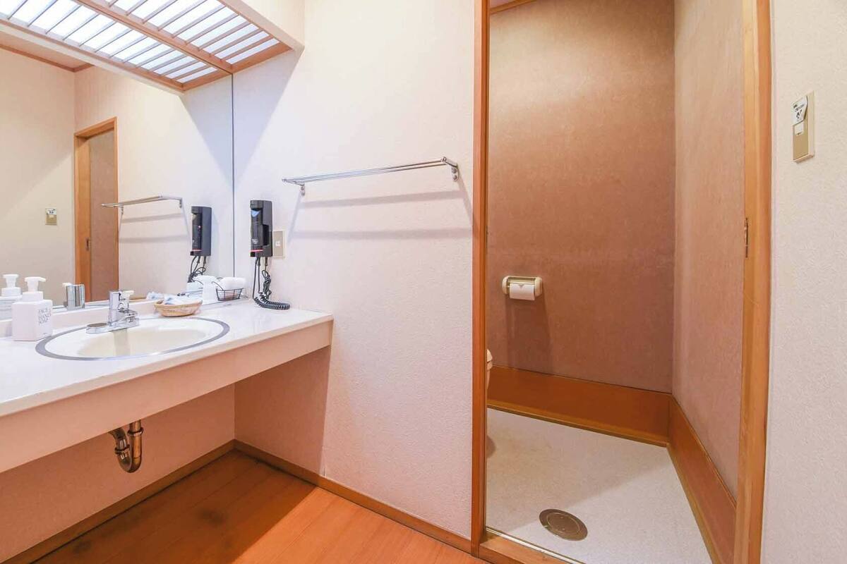 A bathroom with a sink, mirror, hand soap dispenser, and a glass shower stall.