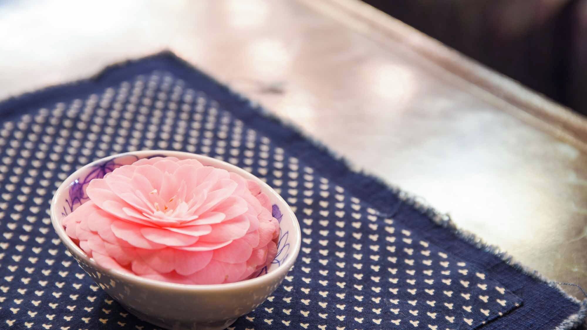 A bowl of pink flower petals on a patterned cloth.