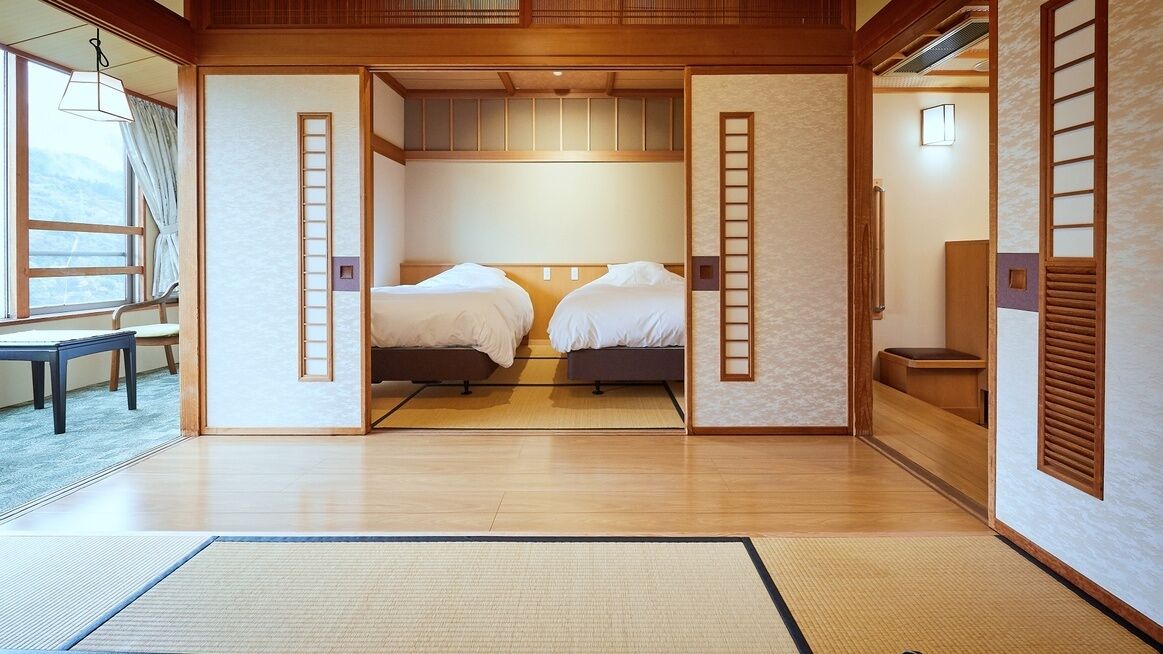 A traditional Japanese-style room with tatami flooring, two beds, sliding doors, and a view of the outside.