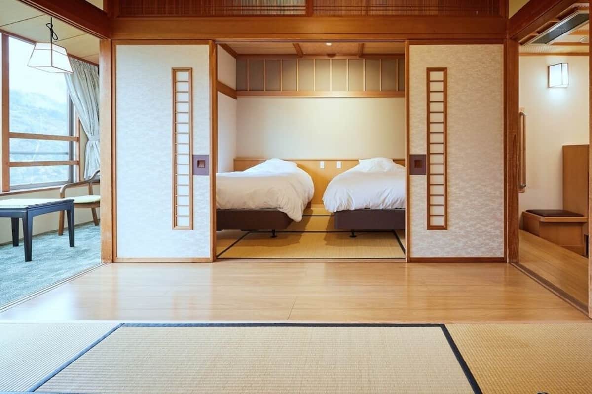 A traditional Japanese-style room with tatami flooring, two beds, sliding doors, and a view of the outside.