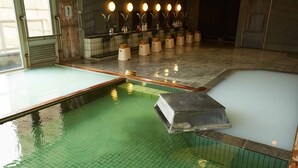 Un onsen japonés tradicional con varias zonas de baño, suelo de baldosas y un banco de madera.