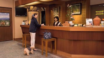 A reception desk with two staff members, a small table with a handbag, and a dog.