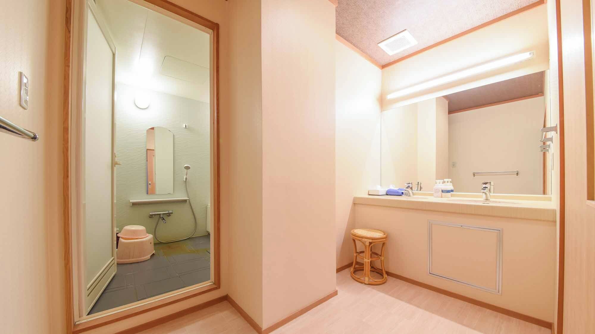 A hotel bathroom with a glass door, a sink with a mirror, and a small stool.