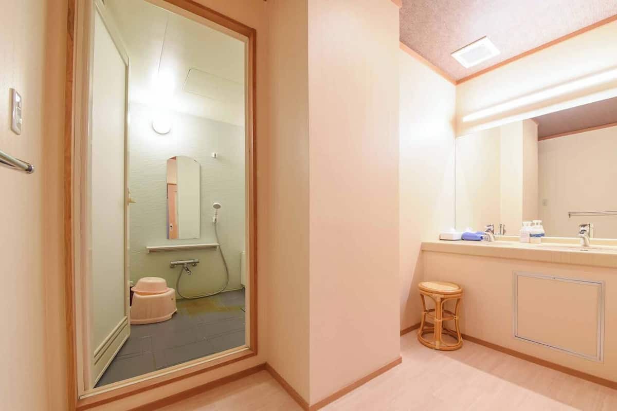 A hotel bathroom with a glass door, a sink with a mirror, and a small stool.
