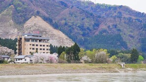 A hotel with a multi-story building, located near a river with a mountainous backdrop. - Aga No Megumi Bousenkaku (Gosen)