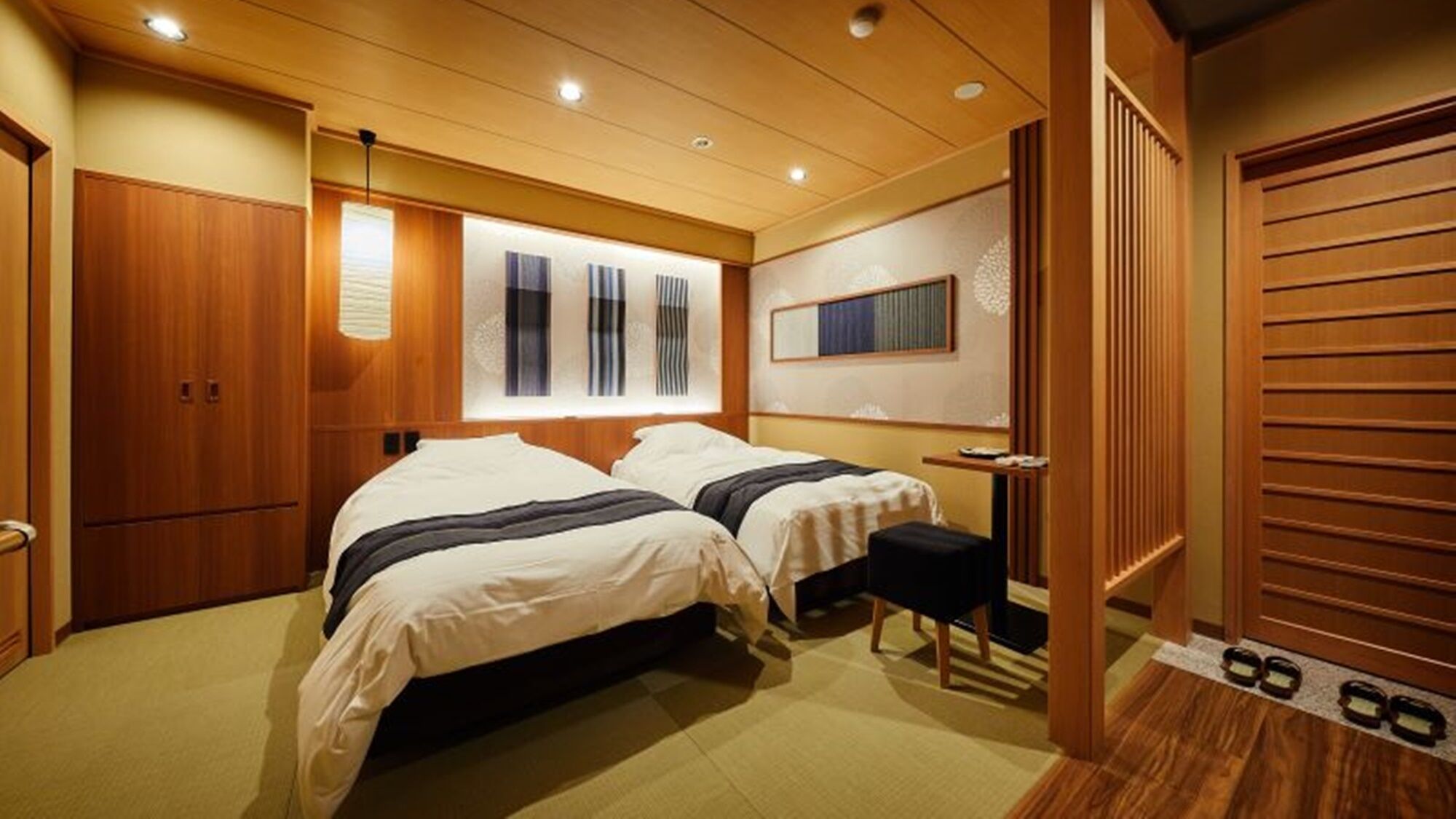 A hotel room with two beds, a wooden wardrobe, a small table, and a mirror.