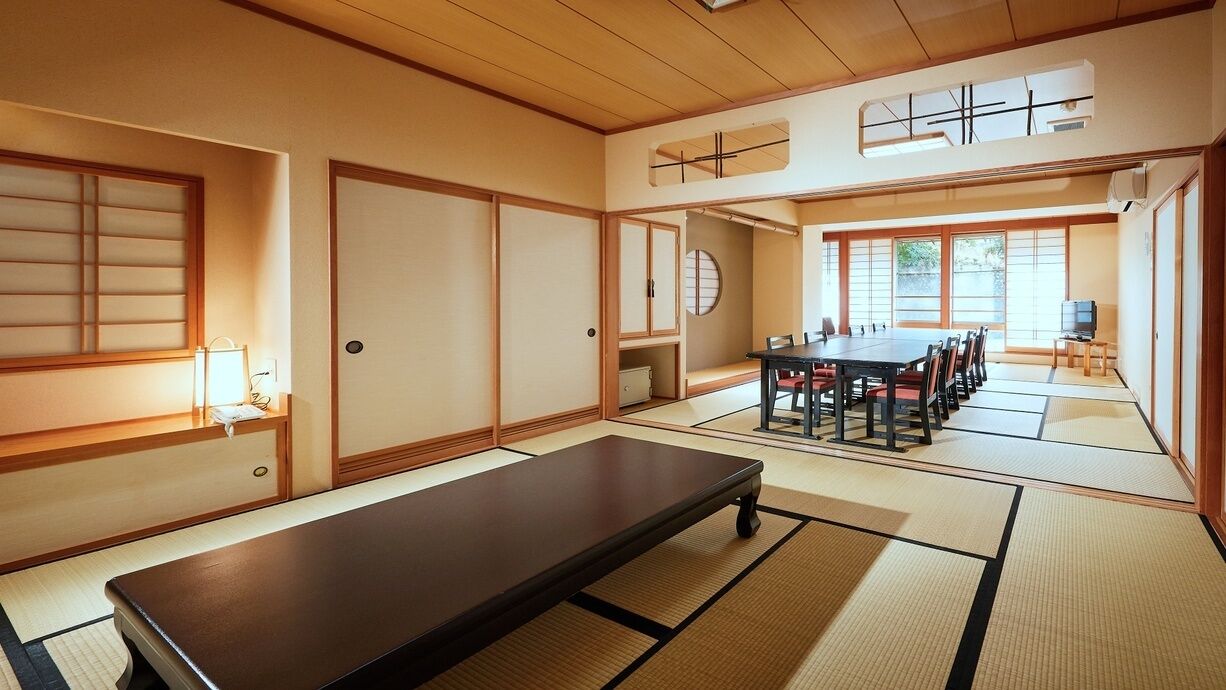 A traditional Japanese room with tatami flooring, a low table, a tatami mat seating area, sliding doors, and a television.