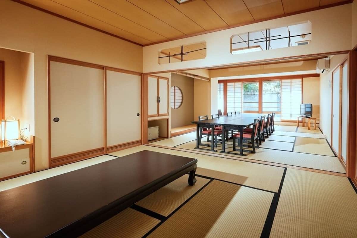 A traditional Japanese room with tatami flooring, a low table, a tatami mat seating area, sliding doors, and a television.
