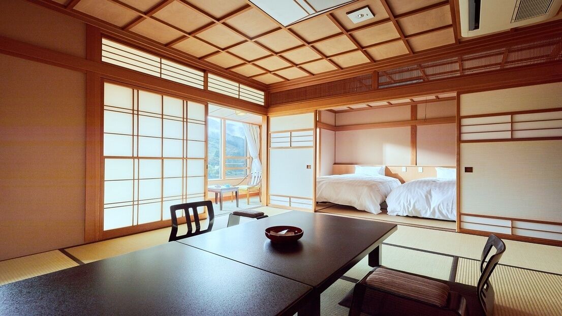 A traditional Japanese room with tatami flooring, a low table, a bed with white bedding, and sliding doors.