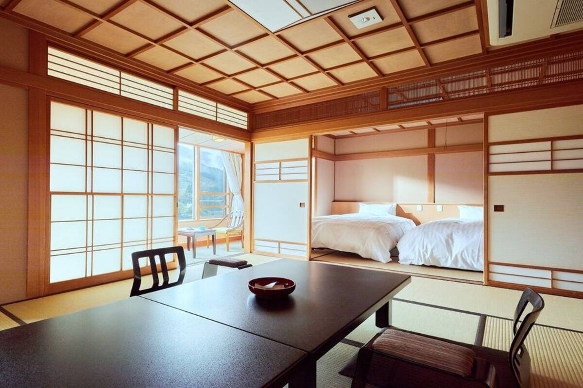 A traditional Japanese room with tatami flooring, a low table, a bed with white bedding, and sliding doors.