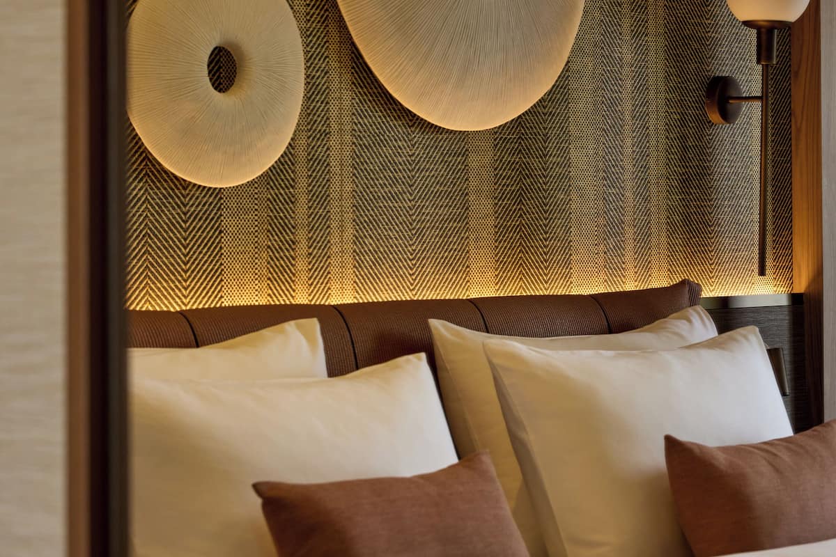 A hotel room with a bed, pillows, and a wall with decorative circular patterns.