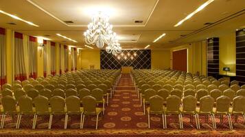 A conference room with rows of chairs, a chandelier, and a patterned carpet.