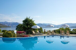Una piscina con sillas de descanso y sombrillas, rodeada de montañas y un lago.
