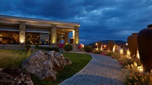 A modern hotel entrance with stone pillars, a paved pathway, and decorative vases. - Limneon Resort & Spa (Kastoria)
