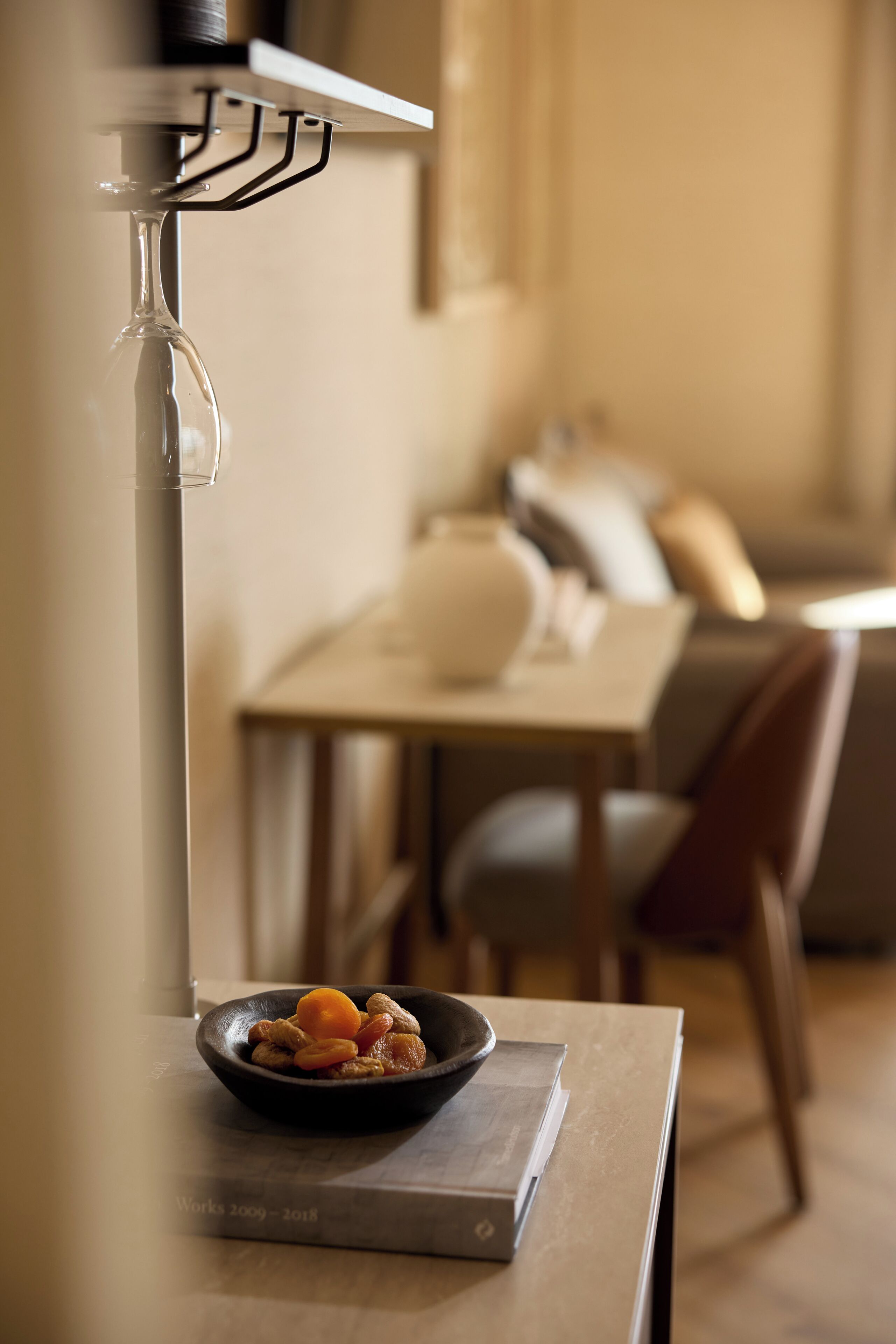 Uma sala de jantar com uma mesa, uma tigela de frutas e uma taça de vinho em um suporte.